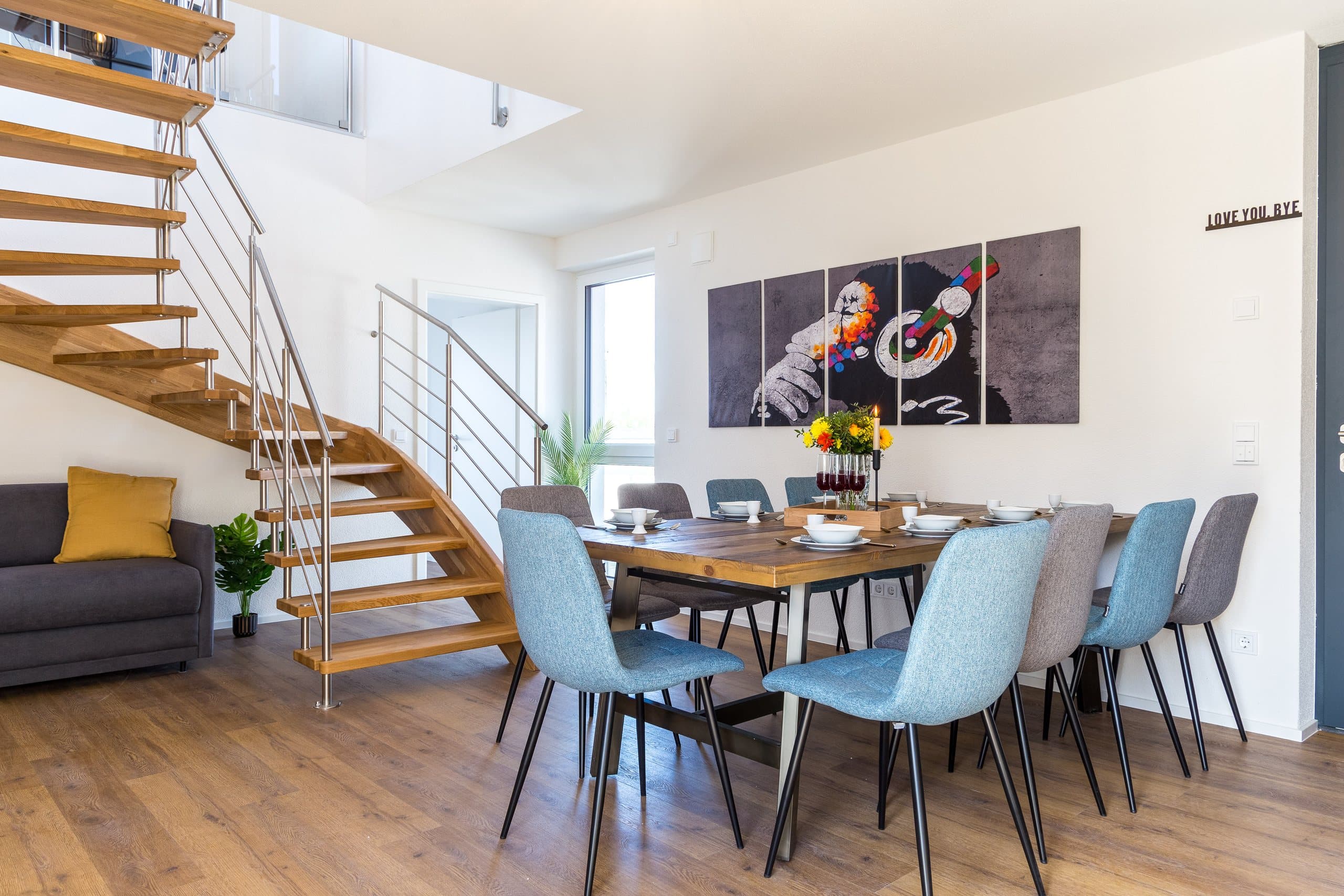 Dining area with a wooden table, blue chairs and an open staircase